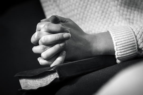Kobieta modli się z założonymi rękoma na Biblii - Zdjęcie, obraz