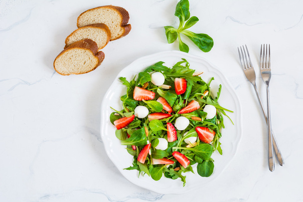 Fresh green salad with arugula, strawberries and spinach on white plate on white background - Foto, afbeelding