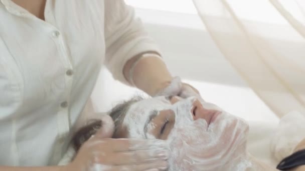 Cerca de manos cosmetólogas, frotar la cara en la máscara en la cara de chica en salón de belleza
 - Metraje, vídeo