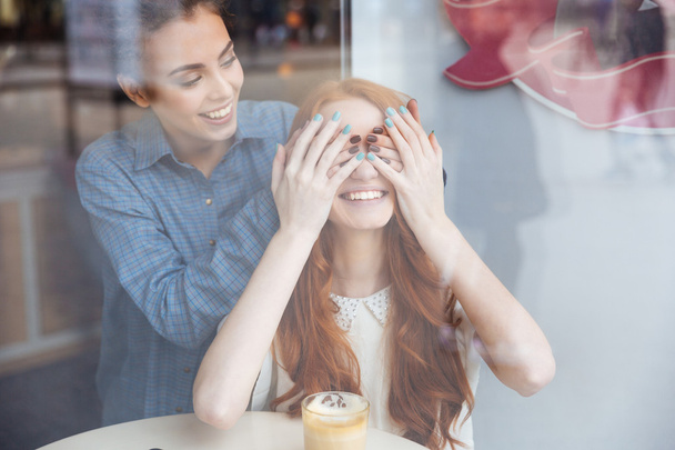 Woman covered eyes by hands to girl sitting in cafe - Photo, Image