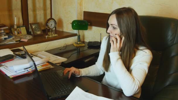 Interesu mówić na telefon i czyta dokument i pracy na laptopie w jej biurze - Materiał filmowy, wideo