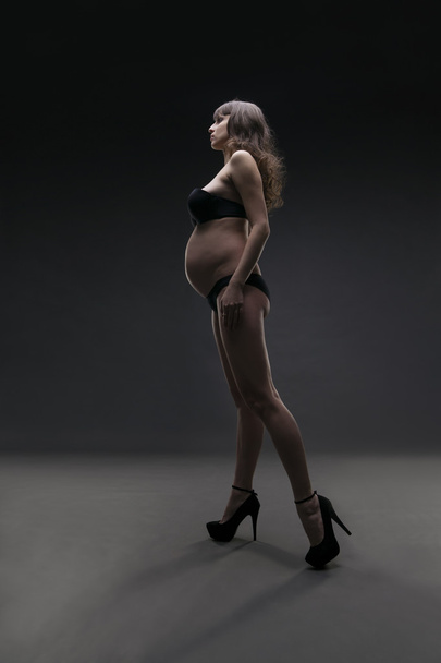 Young beauty and sexy caucasian pregnant woman in black lingerie on gray studio background - Фото, изображение