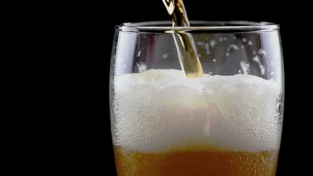 fresh beer with foam into glass on black background - Felvétel, videó