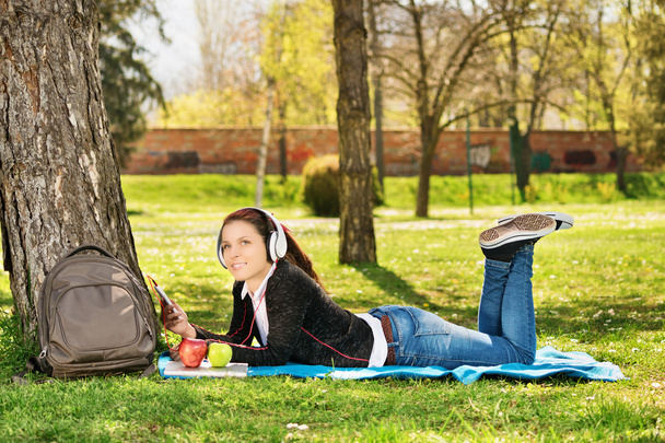 Beautiful female student listening music in the park - Фото, зображення