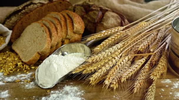 Chléb, snop pšenice uši a mouky na dřevěný stůl, dolly, pohled shora - Záběry, video