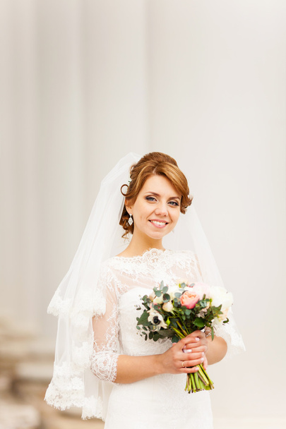 retrato de uma bela noiva jovem que fica entre as colunas e segurando um buquê de noiva
 - Foto, Imagem
