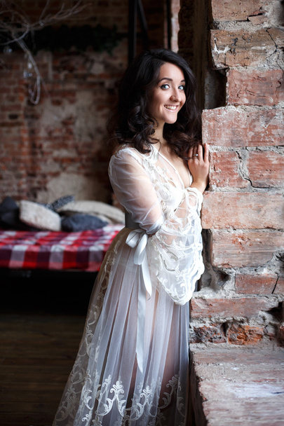 Bride's morning in a loft. Beautiful brunette young woman in a white negligee in a morning - Фото, зображення