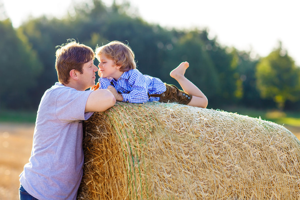 Father and little son having fun on yellow hay field in summer - Foto, immagini