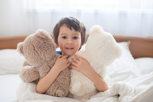 Cute child with teddy bears, lying in bed, looking at camera - Fotografie, Obrázek