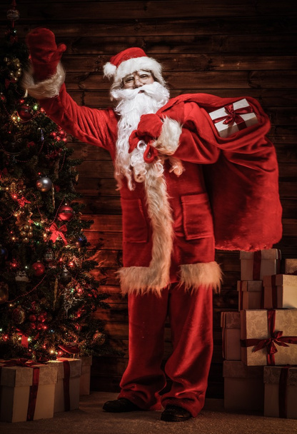 Papai Noel em casa de madeira interior com saco cheio de presentes de Natal
 - Foto, Imagem