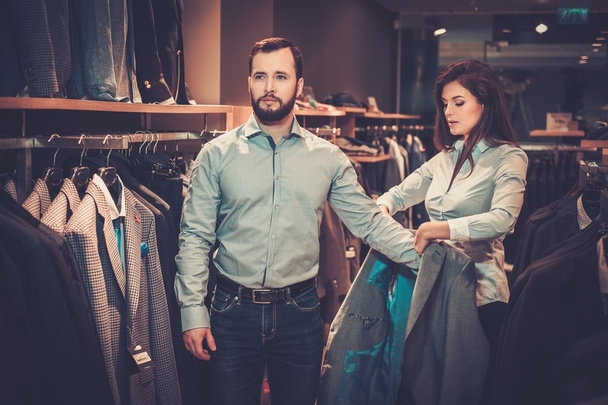 Confident handsome man with beard choosing a jacket in a suit shop. - Fotó, kép