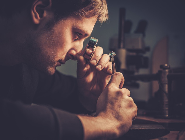 Ювелир смотрит на кольцо через микроскоп в мастерской
.  - Фото, изображение