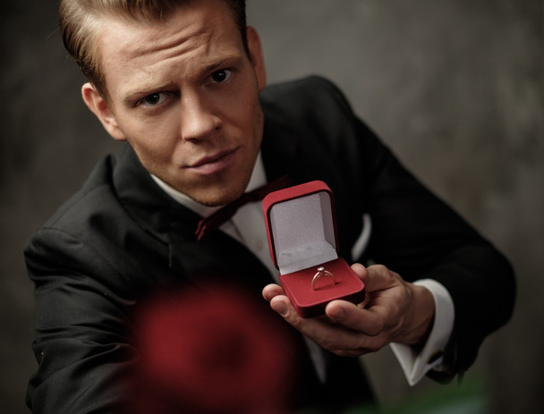 Человек держит коробку с кольцом предложения и красной розой
 - Фото, изображение