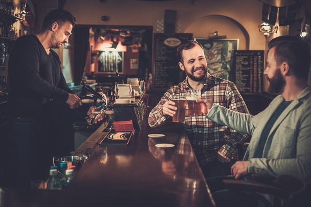 vrienden drinken tapbier op toog in pub. - Foto, afbeelding