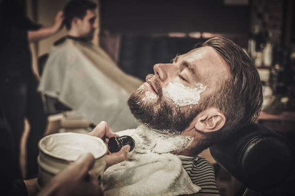 Szakállas ügyfél borotválkozás közben a borbélyüzletben - Fotó, kép