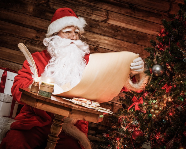 Санта-Клаус в деревянных интерьерах читает список пожеланий
 - Фото, изображение