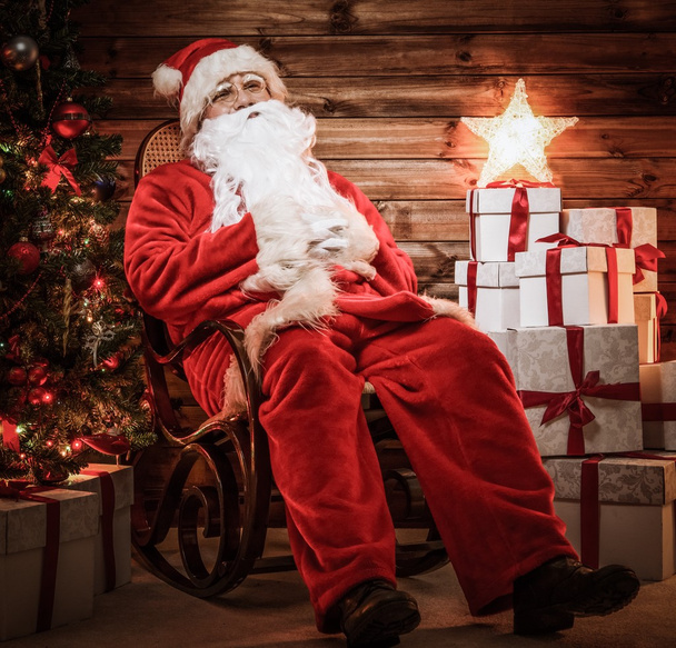 Άγιος Βασίλης κάθεται στο ρηλάξ στο ξύλινο σπίτι εσωτερικό  - Φωτογραφία, εικόνα