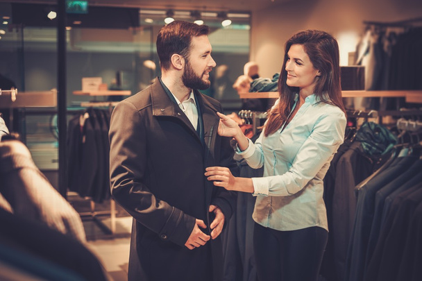 Confident handsome man with beard choosing a coat in a suit shop. - Photo, Image