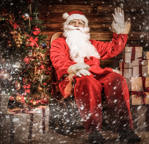 Weihnachtsmann sitzt auf Schaukelstuhl im hölzernen Hausinneren  - Foto, Bild