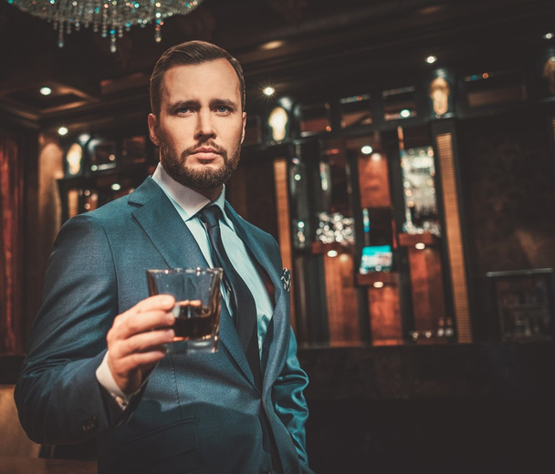 Homme confiant et bien habillé avec un verre de whisky dans un appartement de luxe intérieur
. - Photo, image