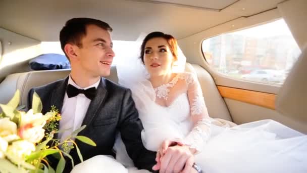 Bride and groom in love sitting on a car, holding hands and talking with each others. - Footage, Video