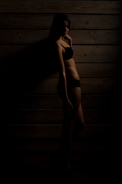 schöne sexy Mädchen in einem schwarzen Badeanzug auf einem Hintergrund aus polierten Brettern - Foto, Bild