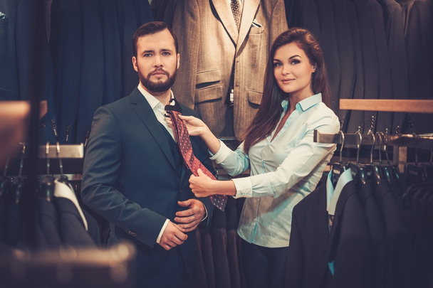 Hombre guapo y seguro con barba eligiendo una corbata en una tienda de trajes
. - Foto, Imagen