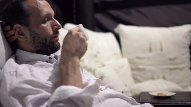 man drinking coffee and relaxing on bed - Imágenes, Vídeo