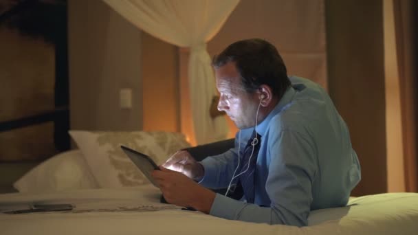Businessman watching film on tablet computer on bed - Metraje, vídeo