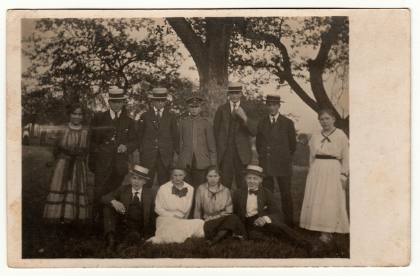 Ein altes Foto zeigt junge Leute, die im Freien posieren. Männer tragen breitkrempigen Hut mit Band und dunklen Anzug. Schwarz-Weiß-Antikfotografie. - Foto, Bild