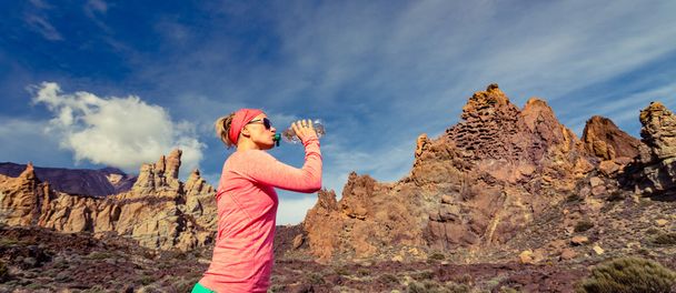 Женщина бегущая по тропе пьет в вдохновляющей горной местности
 - Фото, изображение