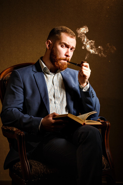 Portrait of handsome young man in blue suit smoking a pipe and read book - Foto, imagen