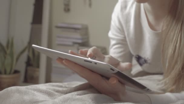 Girl lying on bed at home using tablet, indoors. - Felvétel, videó