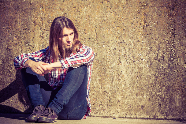 Мужчина с длинными волосами сидит в одиночестве грустный на гранж-стене
 - Фото, изображение