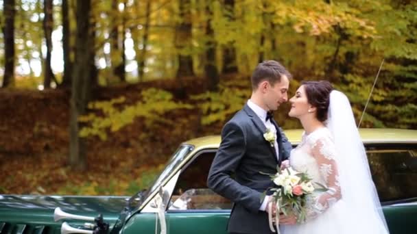 Belo casal apenas casado beijando uns aos outros na frente de um carro retro verde no parque
. - Filmagem, Vídeo