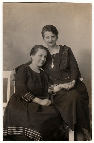 La foto vintage muestra a las mujeres posando en un estudio fotográfico. Se sientan en el banco histórico blanco. Fotografía antigua en blanco y negro
. - Foto, imagen