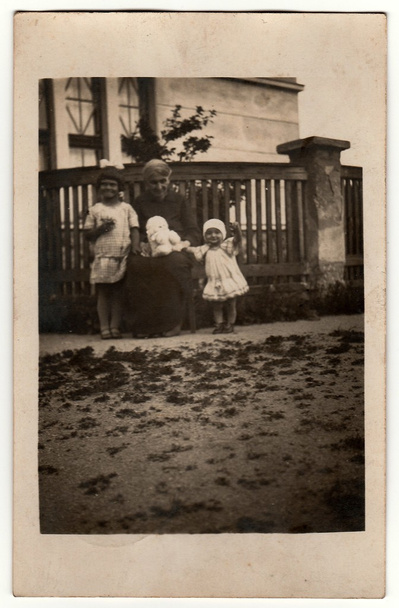 La foto de Vinatge muestra a mujeres y niños posando frente a la casa. La mujer sostiene el oso de peluche. Foto antigua en blanco y negro
. - Foto, imagen