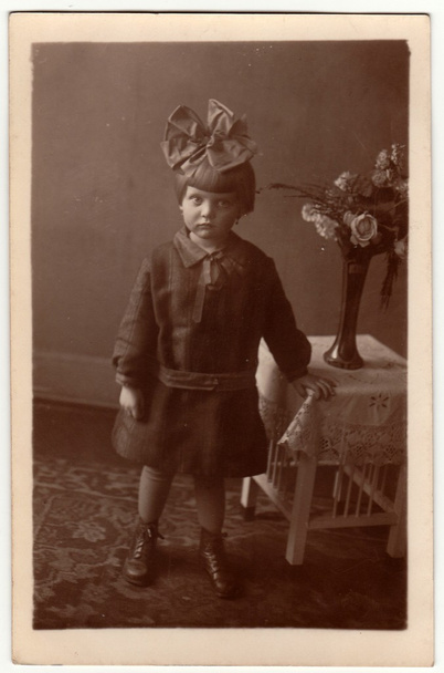 Archiwalne zdjęcie pokazuje, że mała dziewczynka nosi włosy wstążki, stwarza pomieszczeniu. Czarna idealna biały studio fotografii. - Zdjęcie, obraz