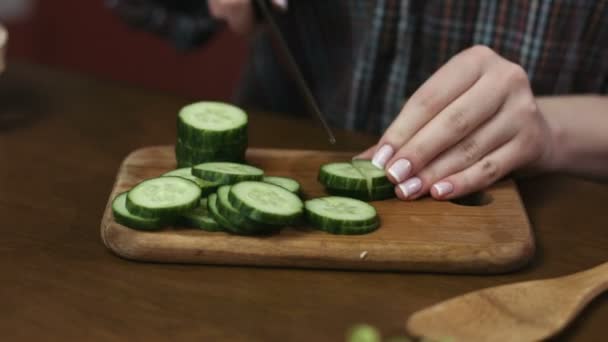 Vrouw met mooie nagels knippen komkommers ter voorbereiding van een salade op een snijplank. - Video