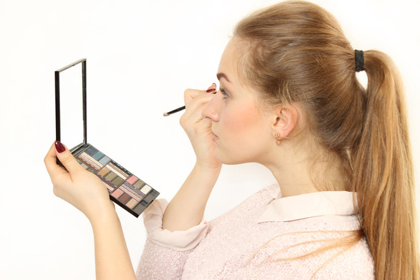 joven chica hace un maquillaje delante de un pequeño espejo cosmético
. - Foto, Imagen