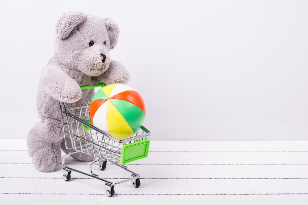 Pequeno carrinho de compras e um ursinho de pelúcia. Imagem conceitual para venda de brinquedos ou fantasias infantis
 - Foto, Imagem
