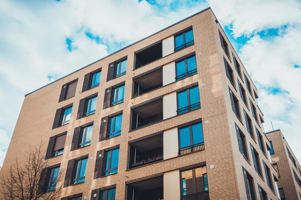 Laag uitzicht op hoge nieuwbouw bruine baksteen appartement complex vierkante ramen en individuele instel patio 's onder de blauwe hemel met witte pluizige wolken in Duitsland - Foto, afbeelding