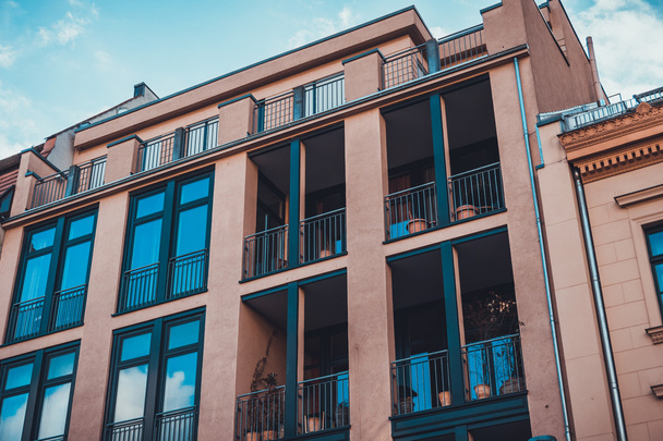 Kum taşı renkli apartman dairesinin düşük açılı görüntüsü. Pencereler mavi gökyüzünü ve verandalı bulutları yansıtıyor. - Fotoğraf, Görsel