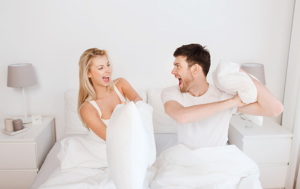 happy couple having pillow fight in bed at home - Foto, Imagem