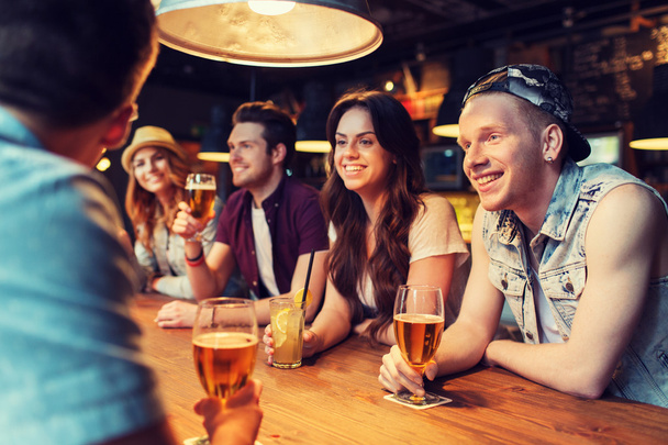 happy friends with drinks talking at bar or pub - Fotoğraf, Görsel