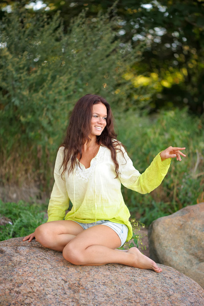 Mujer sonriente sentada en las piedras
 - Foto, Imagen