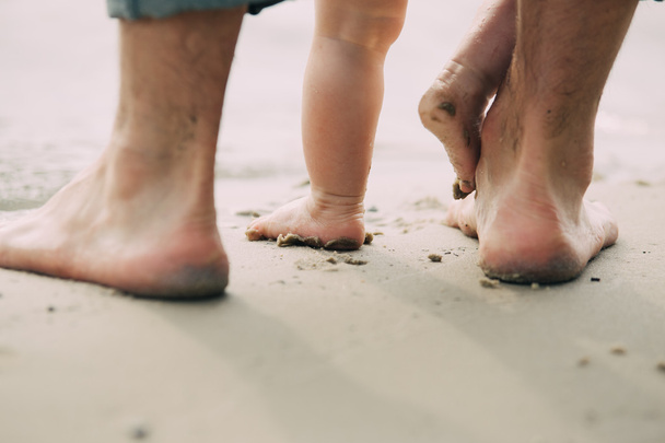 Pies desnudos padre y su pequeño hijo se quedan en la arena cerca del agua
 - Foto, imagen