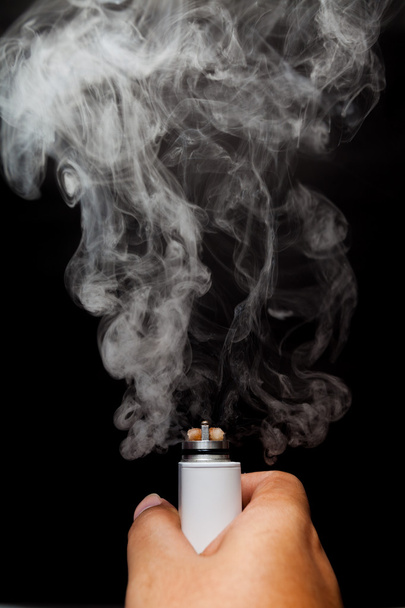 Cigarrillo electrónico o vaper se está activando y liberar una nube en una mano humana, fondo de color negro
 - Foto, Imagen