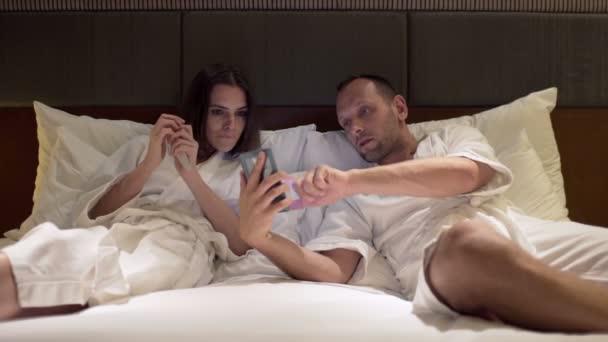 couple talking and using smartphone on bed - Imágenes, Vídeo
