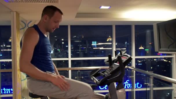 man riding stationary bike in gym - Materiał filmowy, wideo